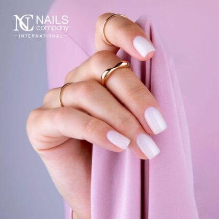 NAILS COMPANY Smart Base Color No. 06 – dłoń z mlecznobiałymi paznokciami i złotymi pierścionkami, logo NC