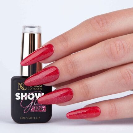 Nails Company Lakier Hybrydowy 124 Show Glow 6 ml - dłoń trzymająca butelkę 6 ml, paznokcie pokryte różowo-czerwonym brokatem