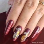 Nails Company Lakier Hybrydowy Sweet Dreams 6 ml. - dłoń z paznokciami w ciemnym bordo z dekoracją złotą i kwiatowym wzorem
